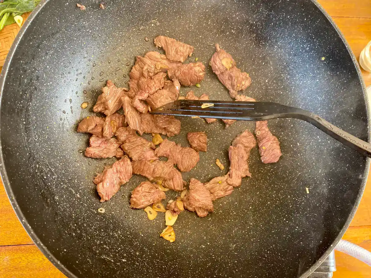 Top-down view of wok pan with golden fried garlic and beef.