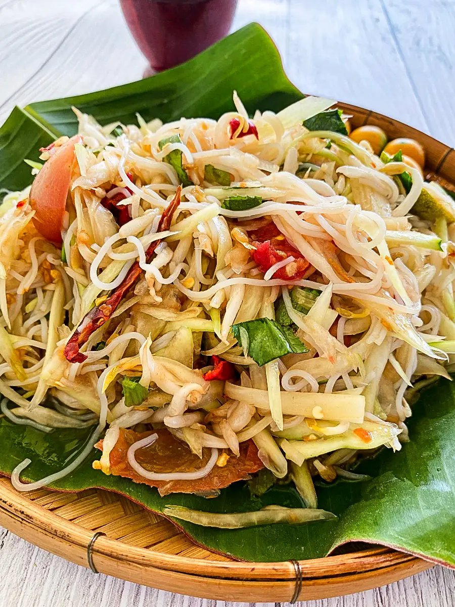 Thai tam sua salad made with shredded green papaya, rice noodles, and herbs, served on a banana leaf with vibrant chili and lime dressing.