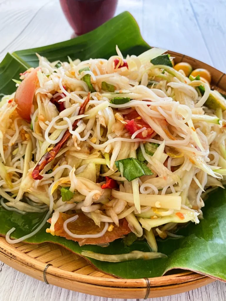Freshly made tam sua Thai papaya salad with vermicelli noodles, chilies, and lime served on a banana leaf.