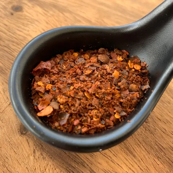 Thai chili flakes in a black spoon on a wooden background.