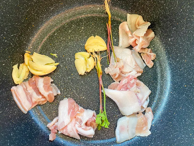 Bacon, garlic, and coriander root cooking in a pot.