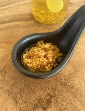 Crispy fried garlic in a black spoon on a wooden cutting board.