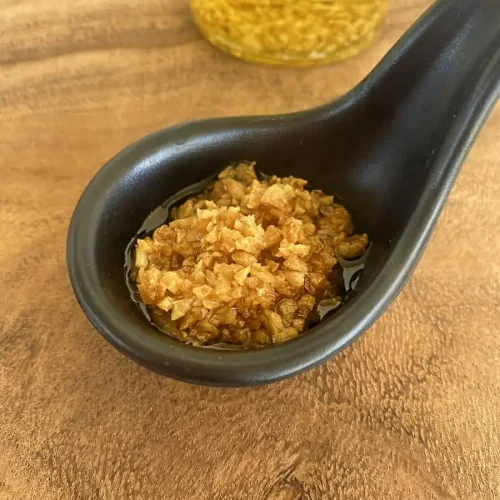Crispy fried garlic in a black spoon on a wooden cutting board.