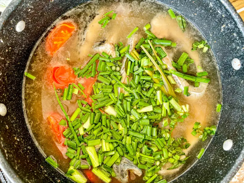 Finished tom yum pla topped with green onions and cilantro in a pot.