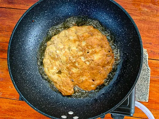 Thai pork omelette frying in hot oil in a pan.