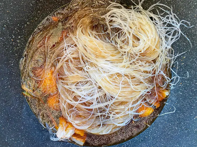 Soaked glass noodles absorbing savory sauce in a pot.