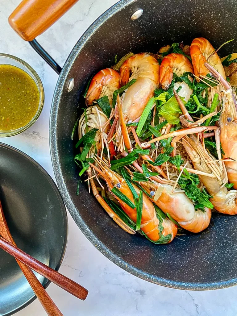 Goong ob woon sen in a pot, showcasing the layering of prawns on top of glass noodles with fresh greens, ready for serving.