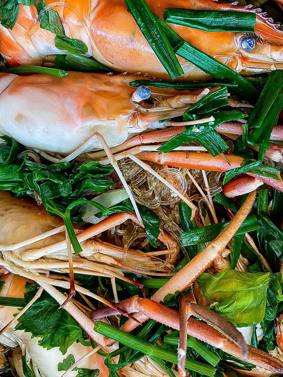 Close-up view of goong ob woonsen in the cooking process, highlighting the succulent prawns nestled among transparent noodles and vegetables.