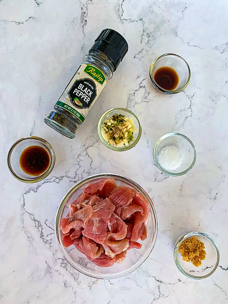 Ingredients for moo gratiem (Thai garlic pork) including sliced pork, garlic, black pepper, soy sauce, and oyster sauce.