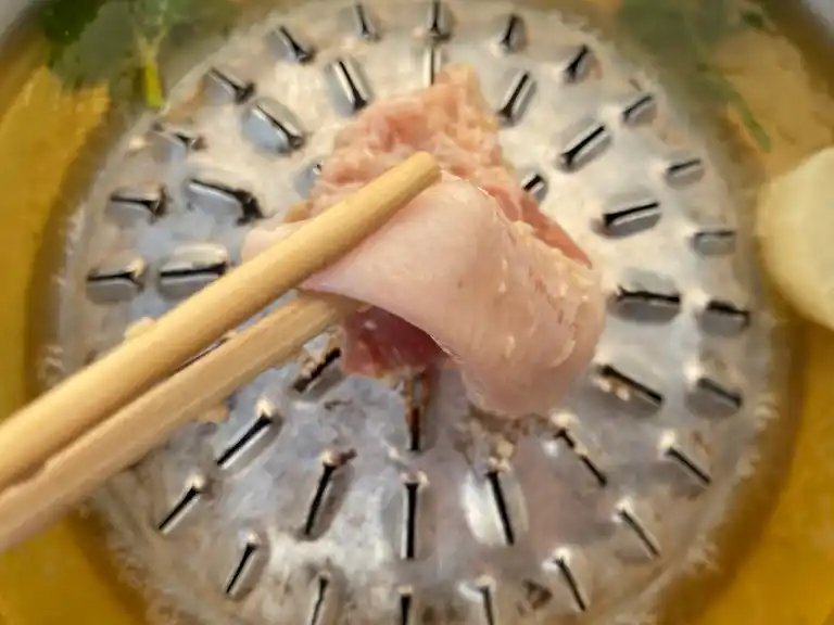 Thinly sliced pork held with chopsticks over a mookata grill.