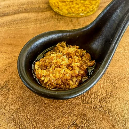 Thai fried garlic in oil served in a black spoon on a wooden table.
