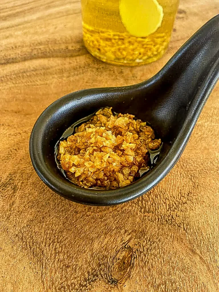 Thai fried garlic in oil served in a black spoon on a wooden table.