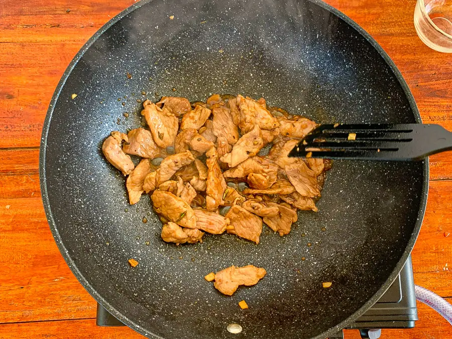Thai garlic pork stir-frying in a wok with savory sauce.