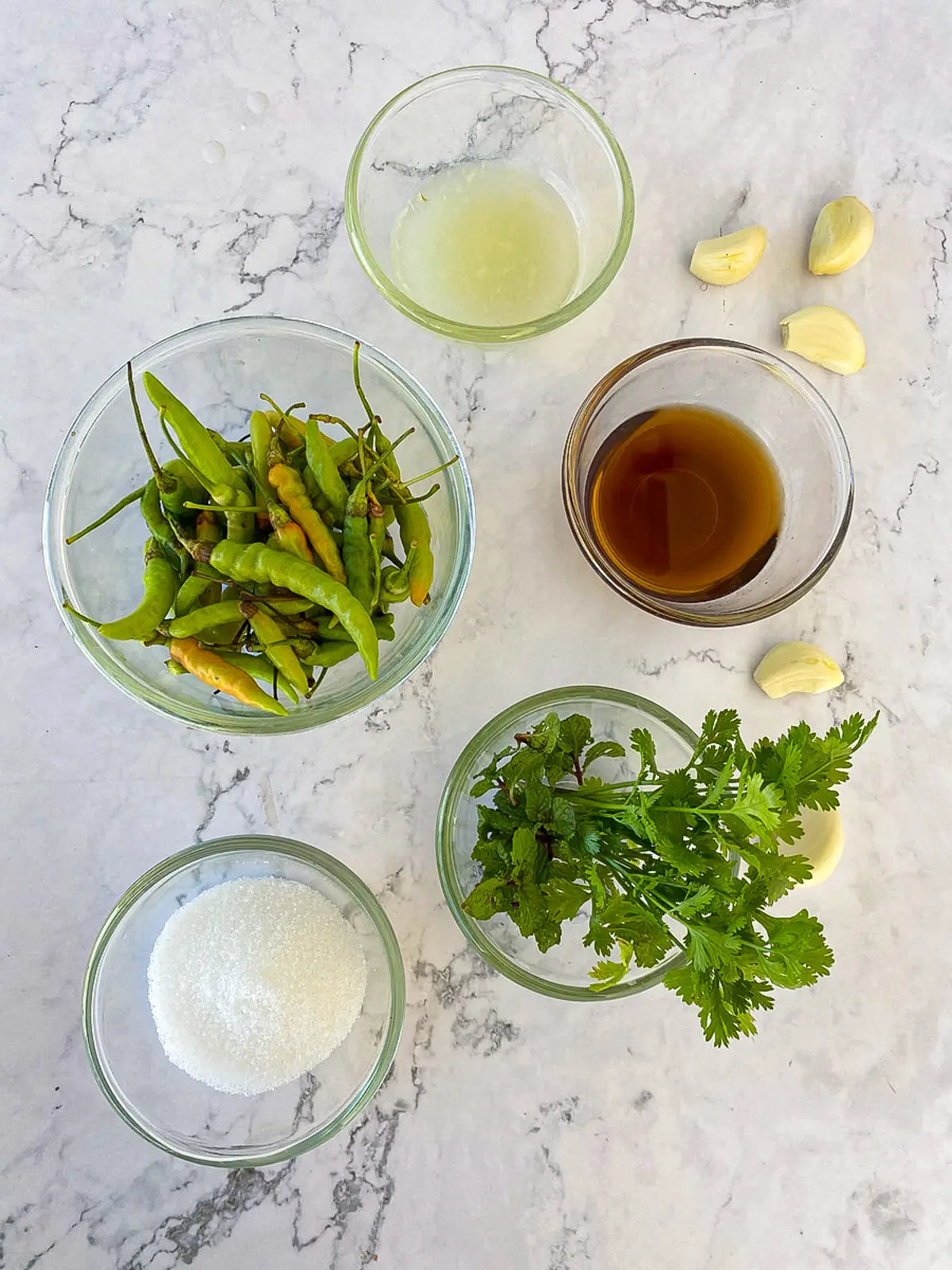 Ingredients for Thai green chili sauce with green chilies, garlic, lime juice, herbs, fish sauce, and sugar.