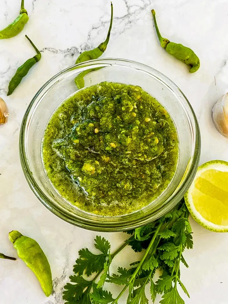 Overhead shot of Thai green seafood sauce with green chilies and fresh herbs spread around it.