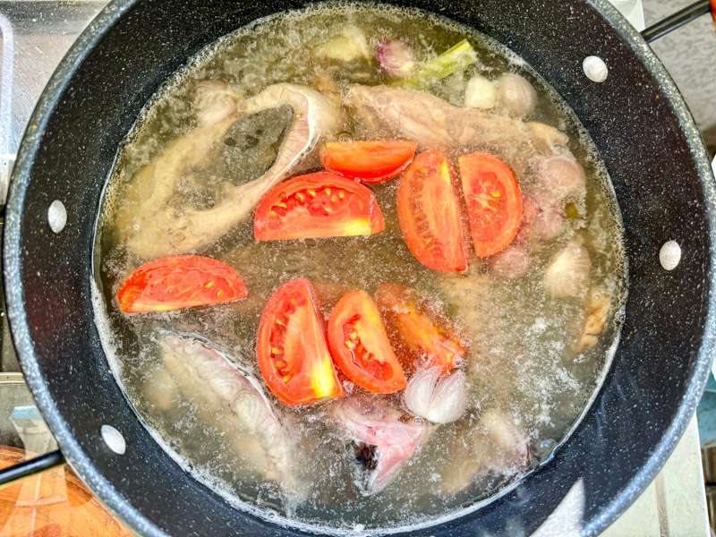White fish and tomatoes simmering in tom yum pla broth.
