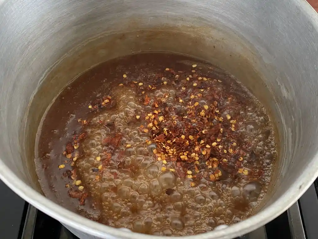 Adding Thai chili flakes to Thai dipping sauce for chicken.