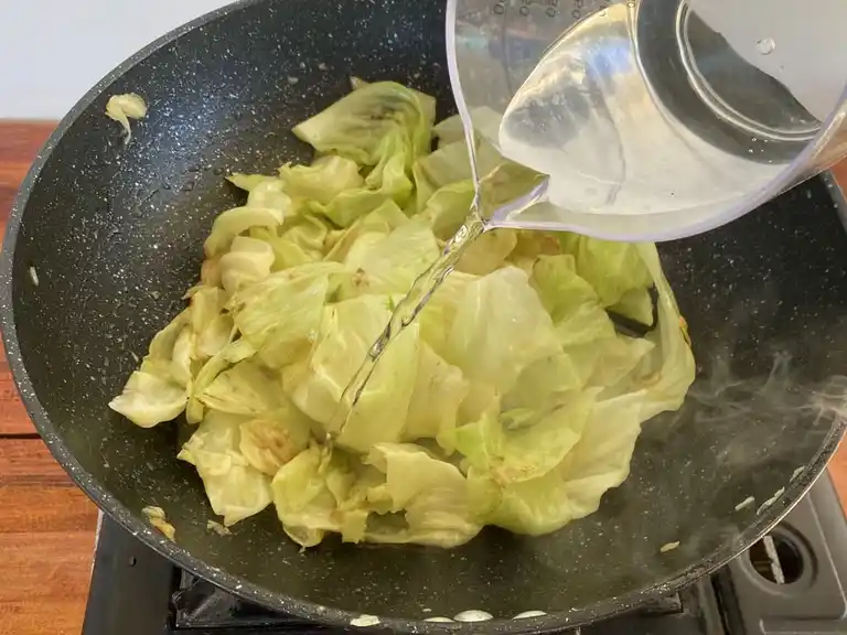 Pouring water into a wok with stir-fried cabbage.