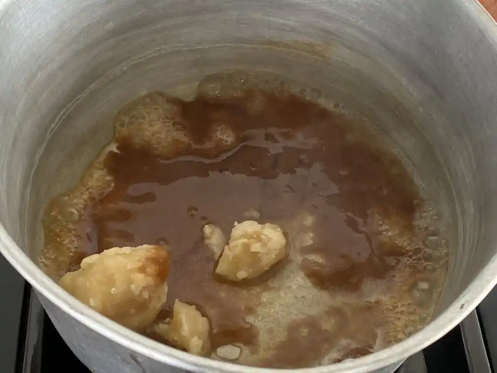 Palm sugar melting into tamarind sauce in a saucepan.