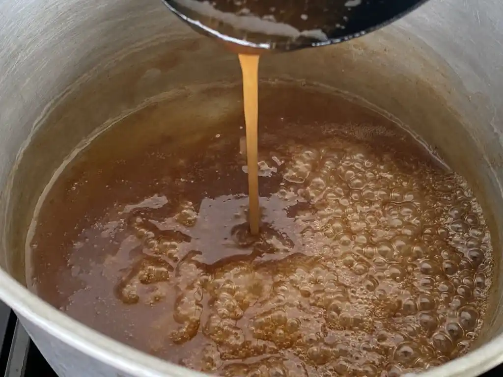 Mixing tamarind paste into Thai dipping sauce for chicken in a saucepan.