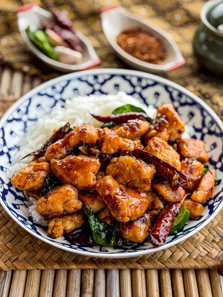 Bowl of pad prik haeng with golden fried chicken, dried chilies, and herbs on a traditional Thai patterned plate.