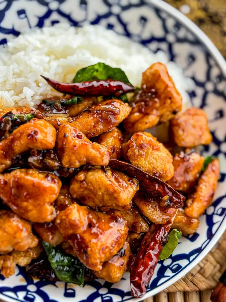 Close-up of Thai crispy chicken stir-fry with dried chilies and kaffir lime leaves, served with jasmine rice.