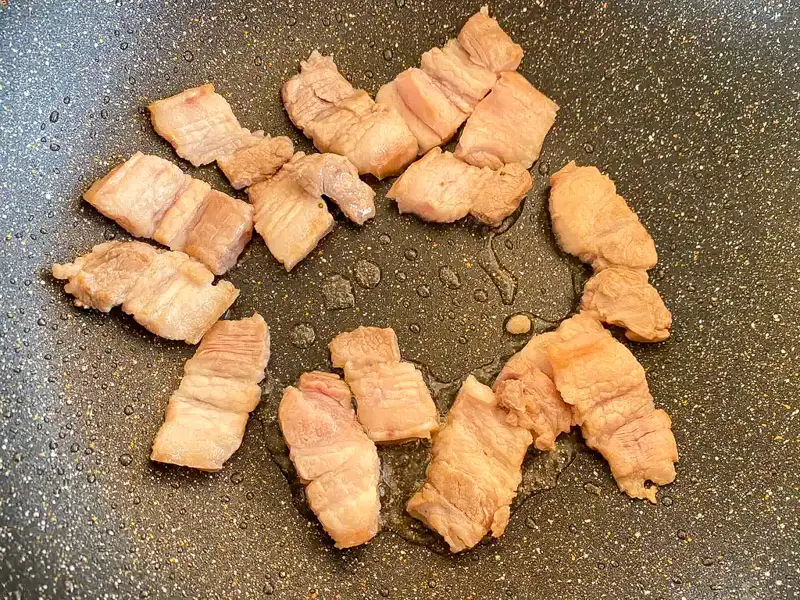 Pork belly browning in a wok.