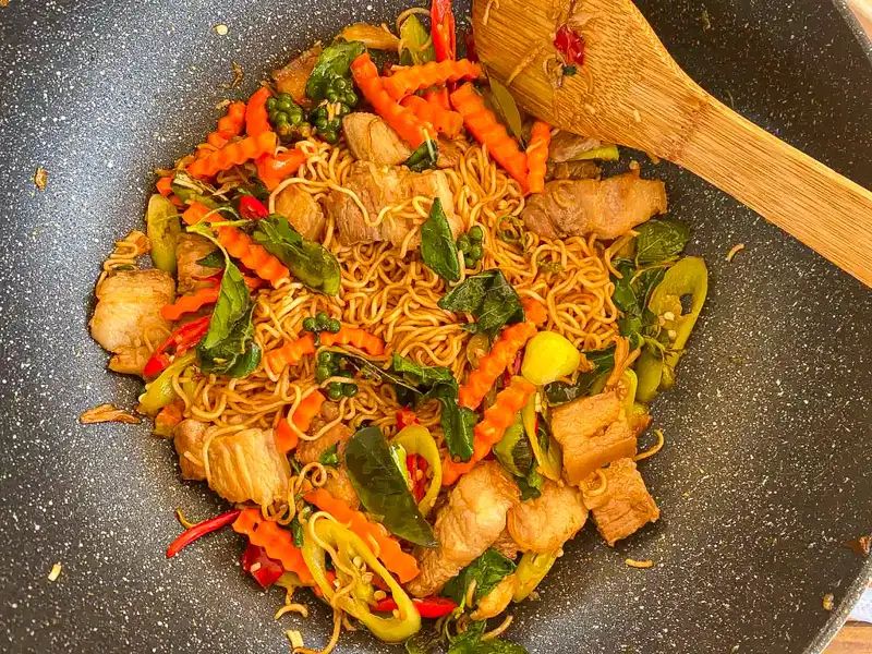 Drunken Mama noodles tossed with pork, vegetables, holy basil, and Thai seasonings in a wok.