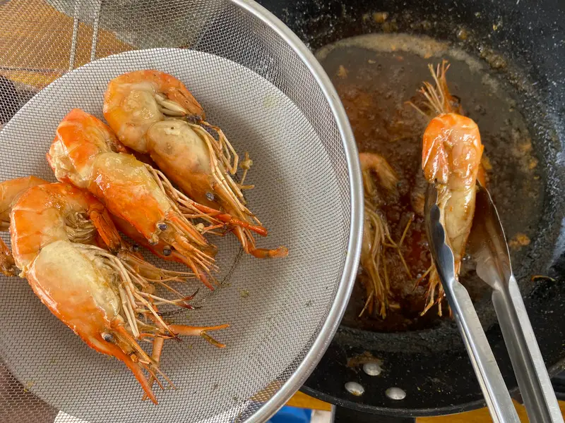 Freshly fried shell-on prawns draining in a mesh colander.
