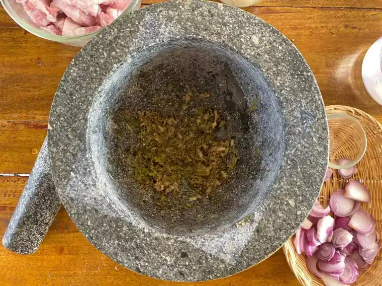 Granite mortar and pestle with finely crushed garlic, peppercorns, and coriander root.