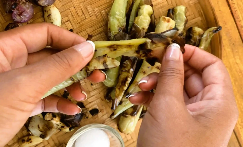Hands removing blackened skin of charred green chilies.