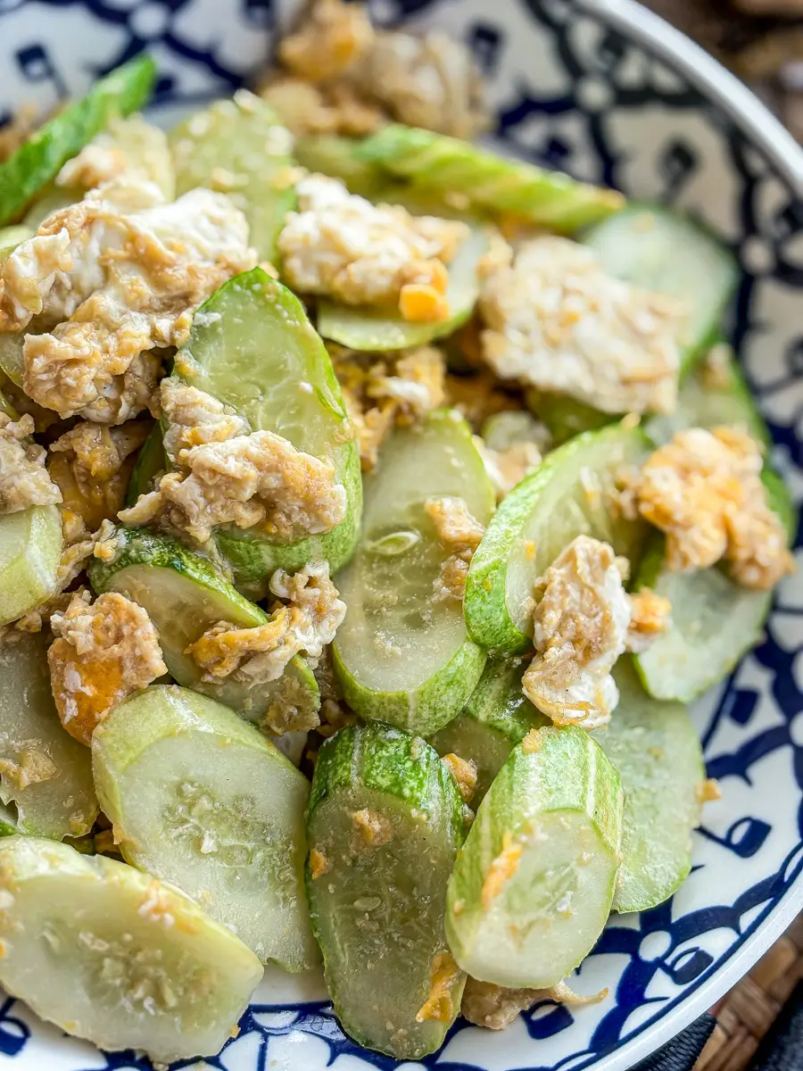 Close-up of stir-fried cucumber with scrambled eggs in a blue and white Thai-style bowl.