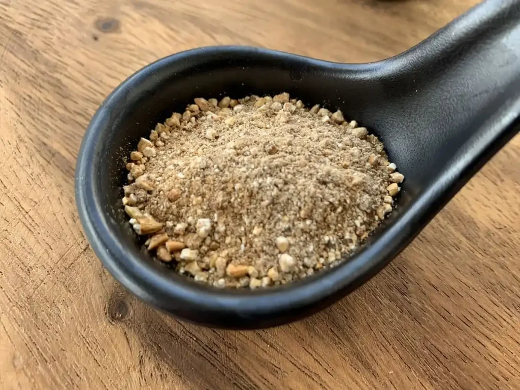 Toasted rice powder in a black spoon on a wooden cutting board.