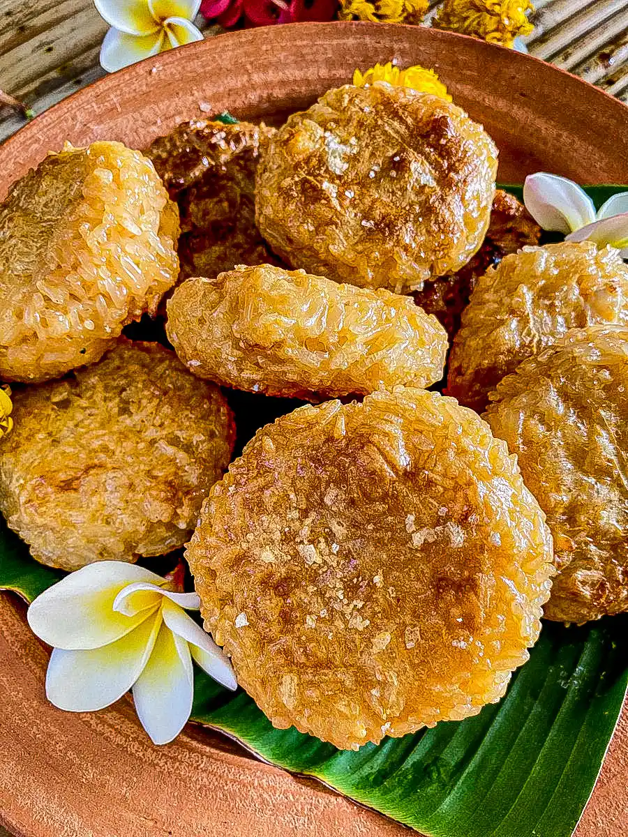 Thai khao jee sticky rice patties grilled to golden brown perfection, arranged on a clay plate with frangipani flowers.