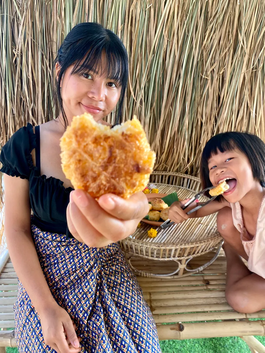Me and my neice eating khao jee (sticky rice with egg) on top of a bamboo table. I am pointing a khao jee that I took a bite of to the camera.