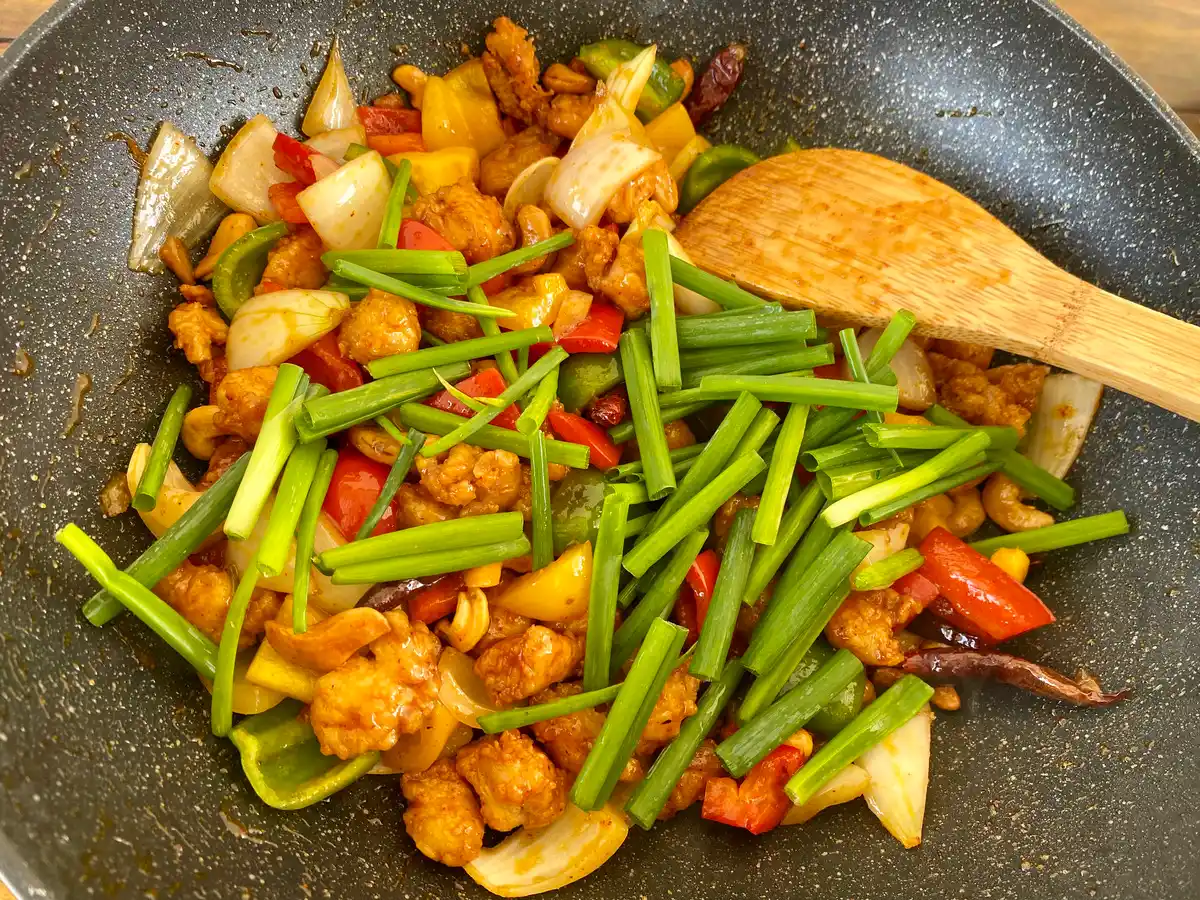 Pan with cashew chicken stir-fry, topped with green onions.