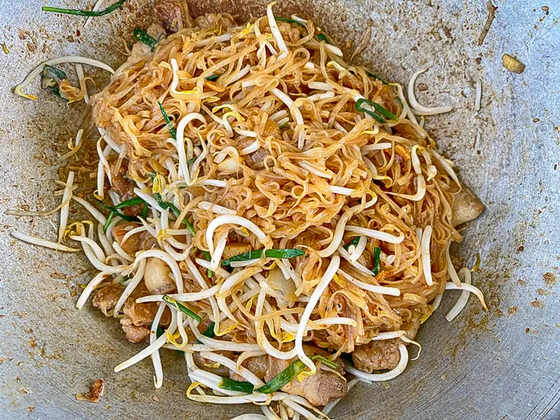 Tossing bean sprouts and green onions into pad mee korat just before serving.