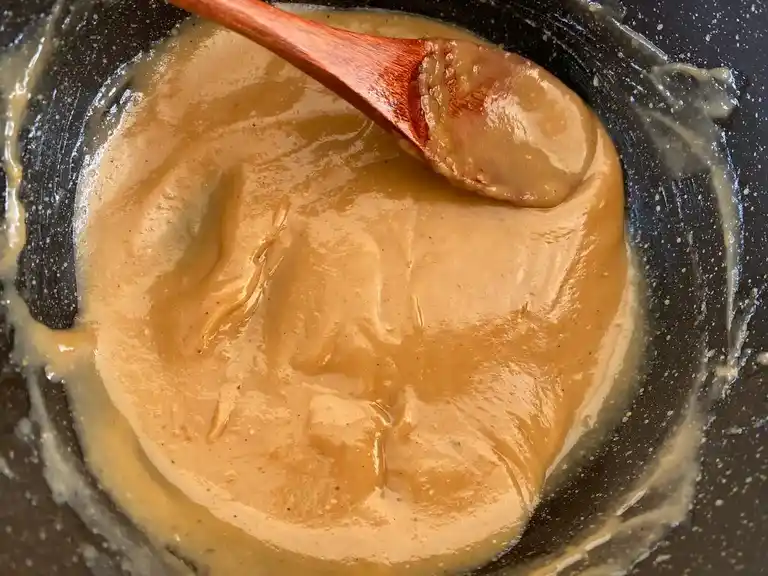 Creamy homemade peanut sauce in a cooking pan with a wooden spoon.