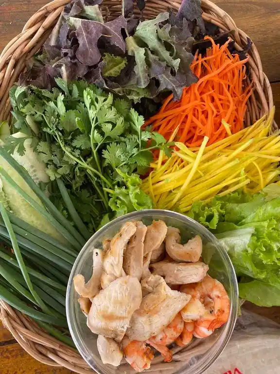 A colorful array of fresh vegetables alongside cooked chicken and shrimp ready for making fresh spring rolls.
