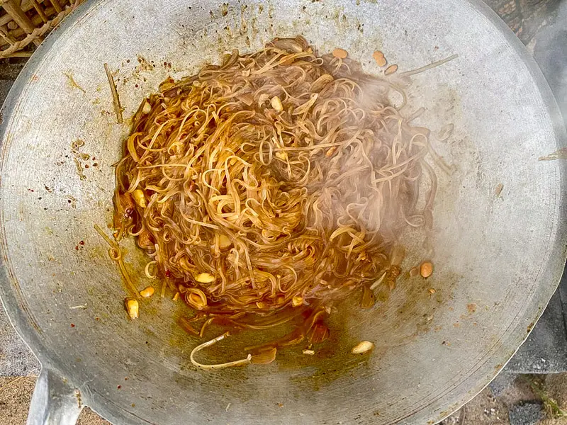 Rice noodles absorbing the pad mee korat sauce in a hot wok before adding the pork and vegetables.