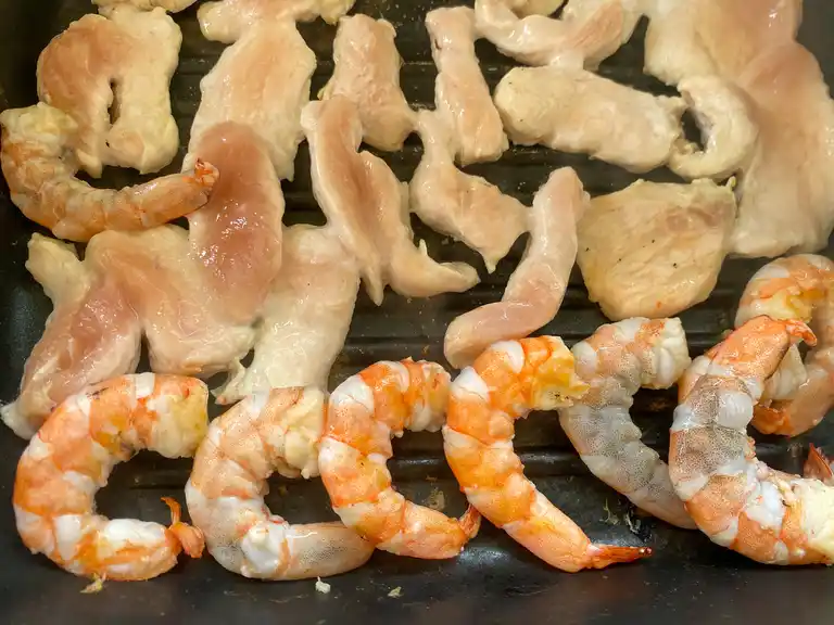 Shrimp and chicken strips being grilled on a stovetop grill pan.