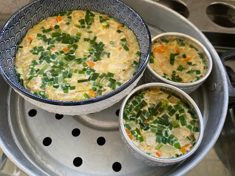 Steaming Thai steamed eggs with vegetables in a traditional steamer.
