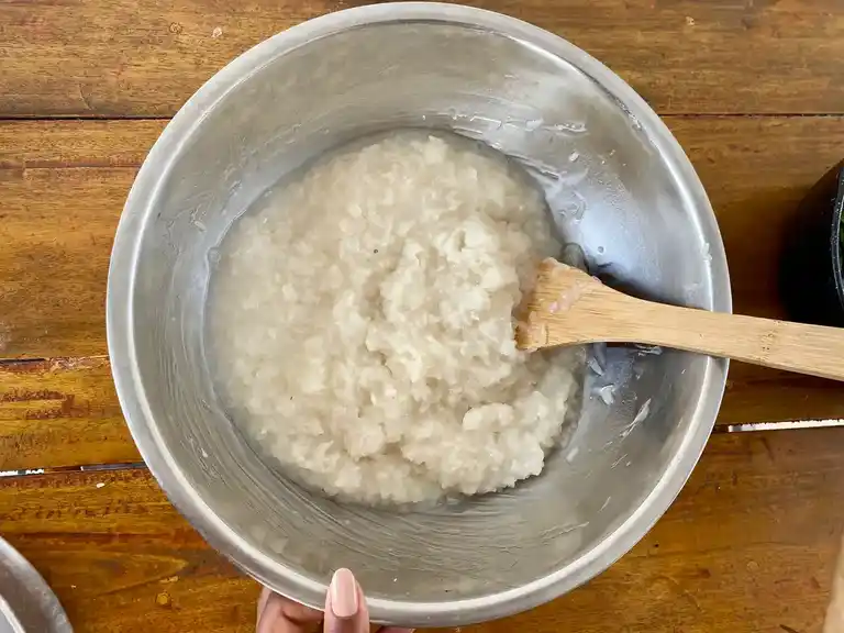 Sticky rice soaked in coconut sauce in mixing bowl with spatula.