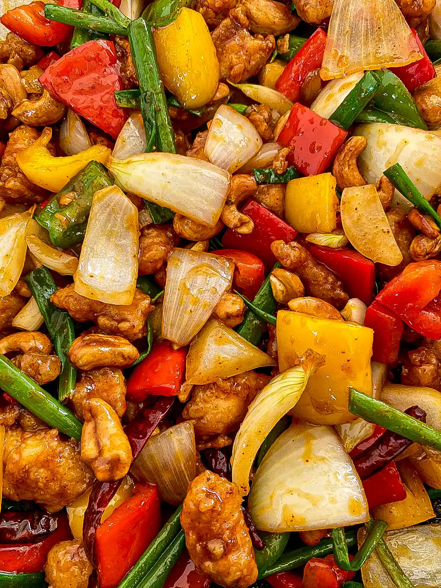 Close-up of Thai cashew chicken stir-fry featuring colorful bell peppers, crunchy chicken, dried chilies, onions, and more.