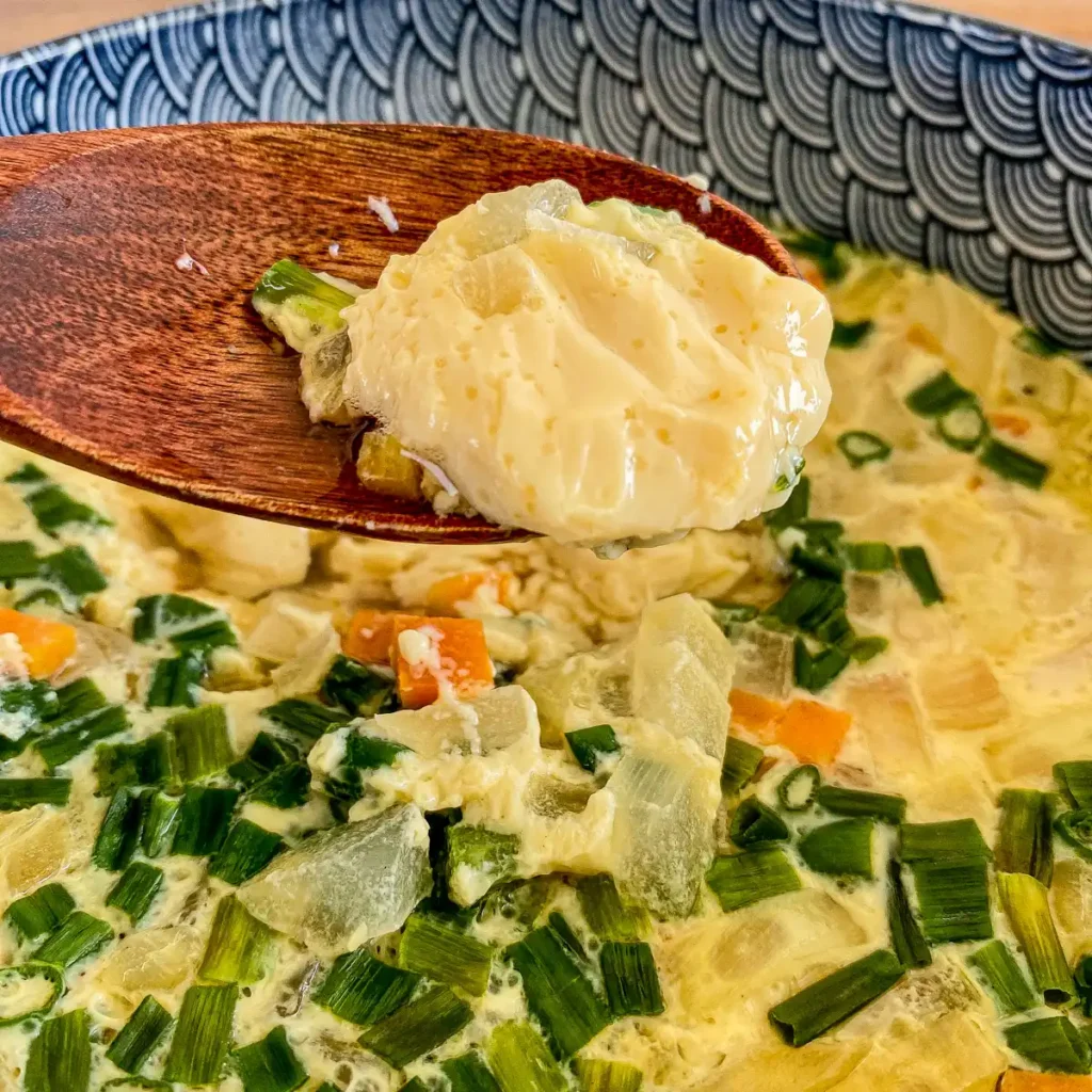 Close-up of Thai steamed egg with vegetables and a wooden spoon is showing the custard-like texture.