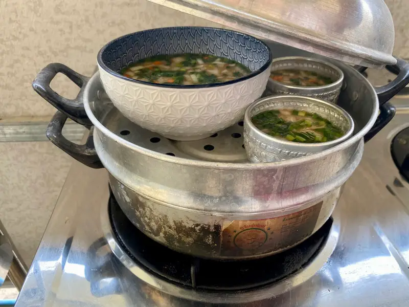 Bowls filled with Thai steamed egg mixture and vegetables, ready to steam.