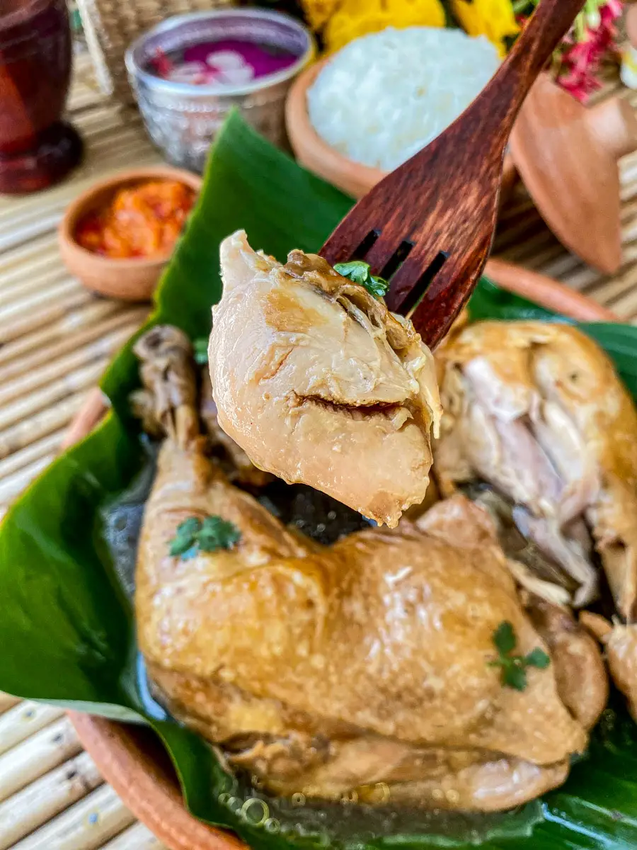 Close-up of a piece of boiled chicken thigh with fish sauce on a fork.