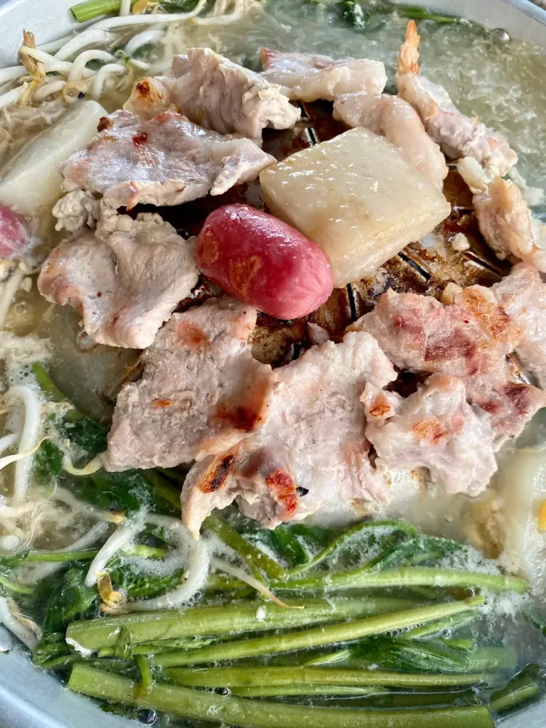 Close-up of meat, vegetables, and glass noodles on a Thai BBQ top.