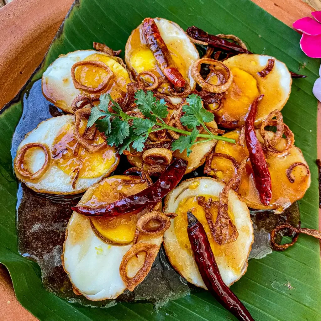 Thai son-in-law eggs topped with sweet tamarind sauce, crispy shallots, and dried chilies on a banana leaf.