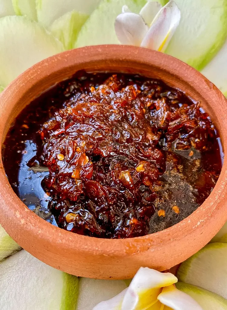 Thai mango dipping sauce in a clay sauce cup, with parts of green mango spread around it.